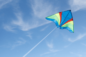 A colorful kite flying in a clear blue sky with wispy clouds.